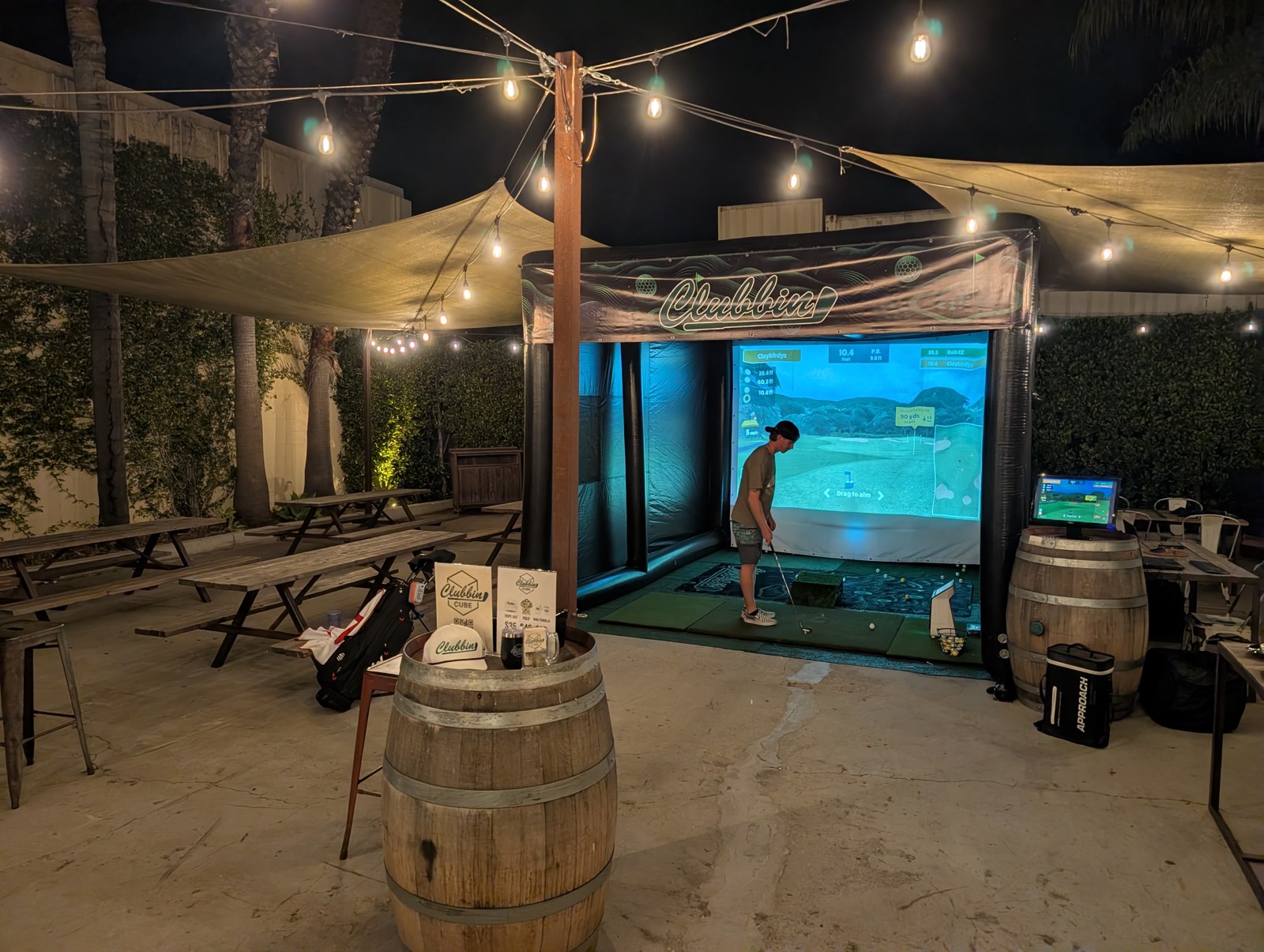 A golfer in the illuminated Clubbin Cube beneath patio string lights