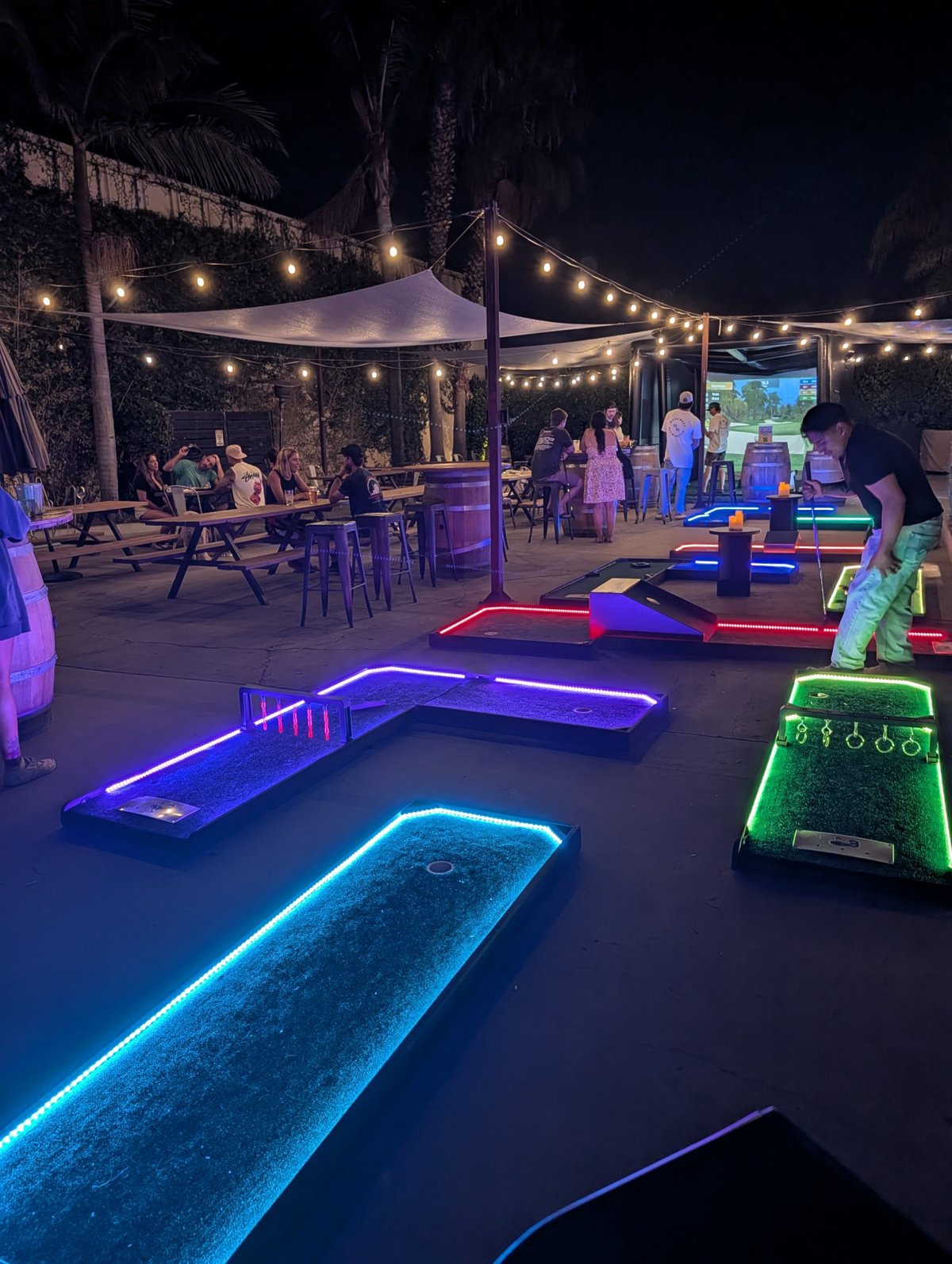 Guests playing neon mini golf beneath string lights and palms at Topa Topa